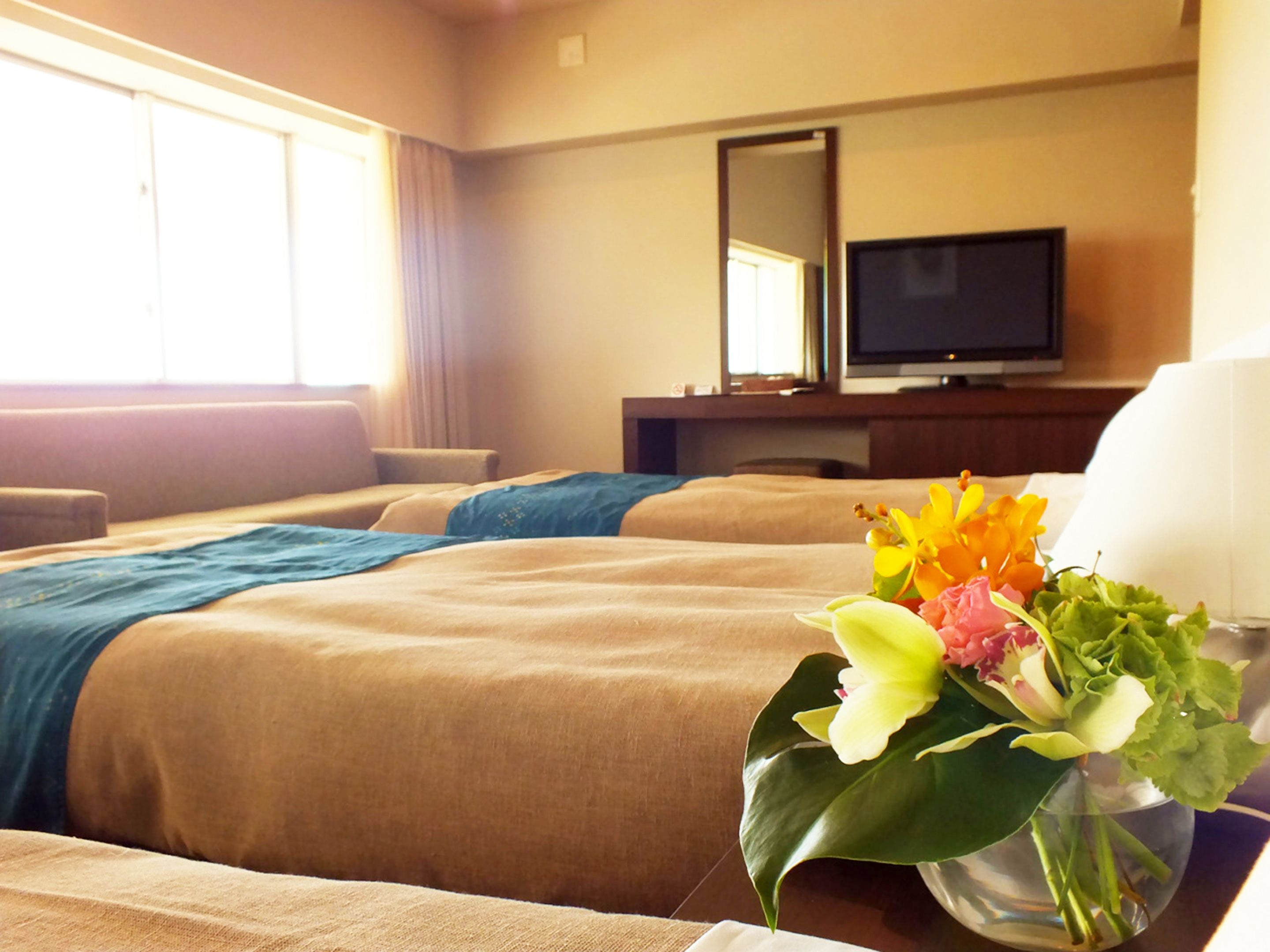 A hotel room with two beds, a TV, and a vase with flowers.