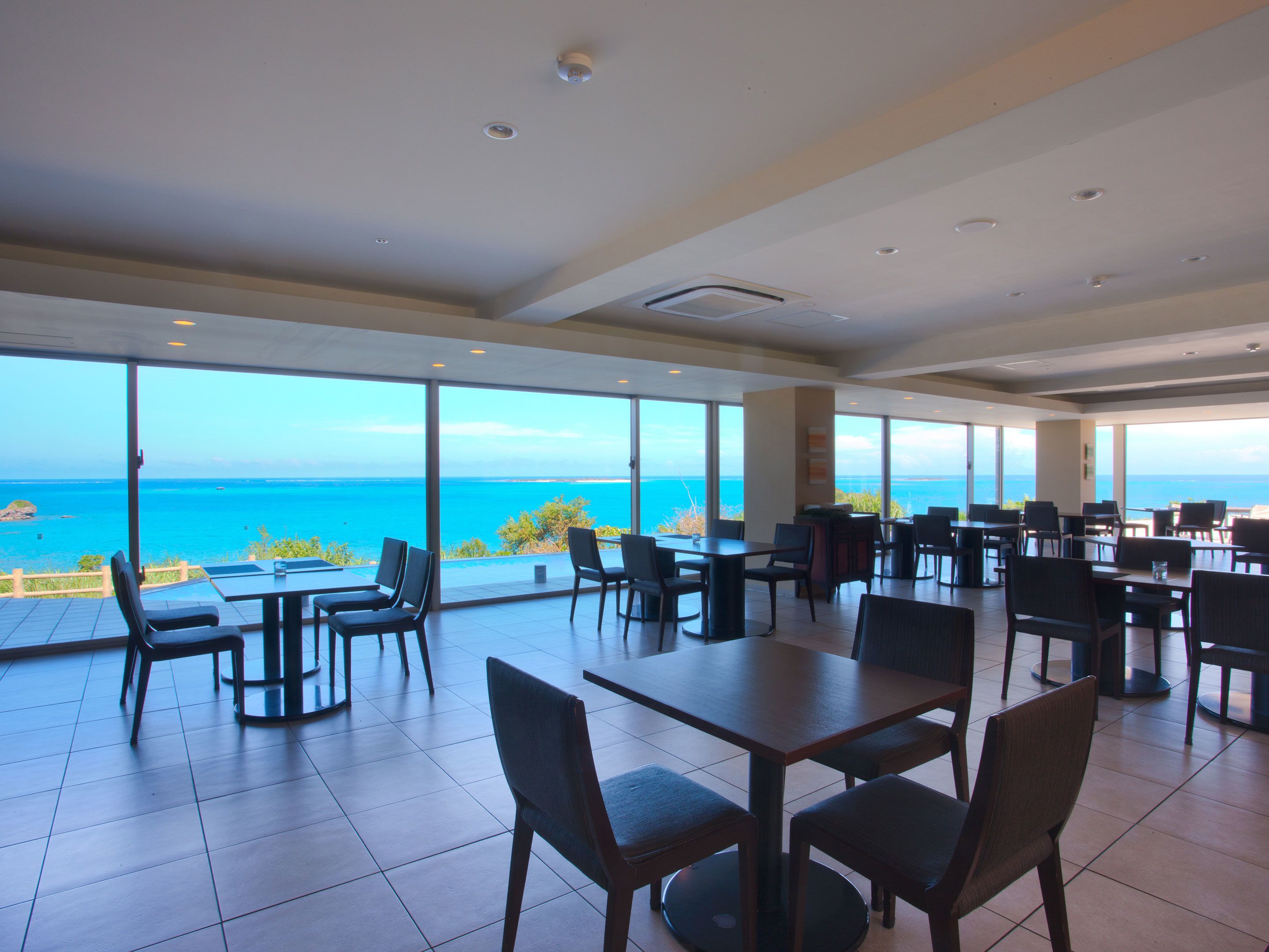 A spacious dining area with large windows offering a view of the ocean. Tables and chairs are arranged for dining.