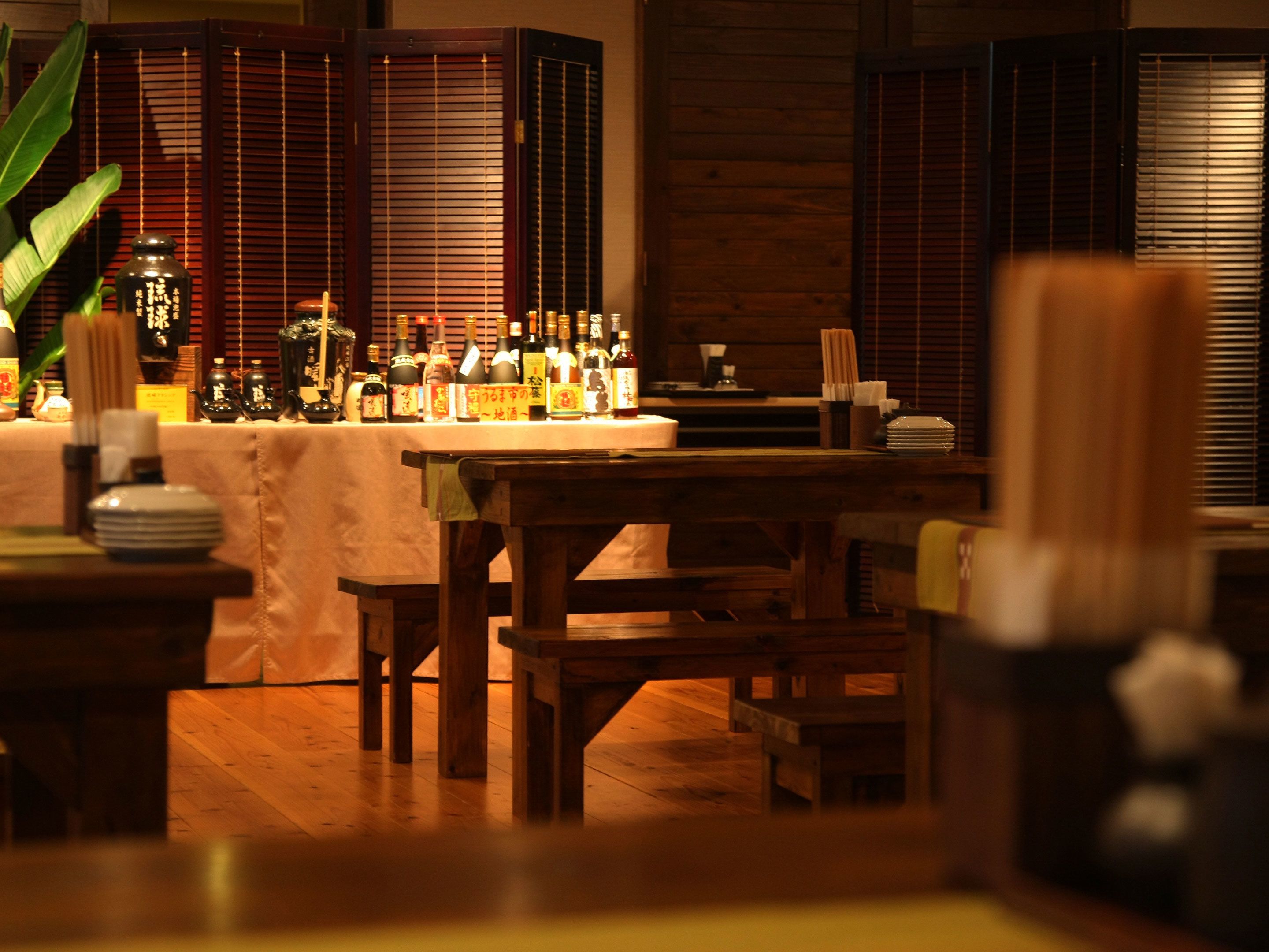 A restaurant interior with wooden furniture, a table with various bottles, and a traditional Asian-style backdrop.