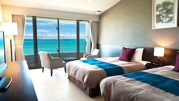 A hotel room with two beds, a desk with a chair, a TV, and a view of the ocean.