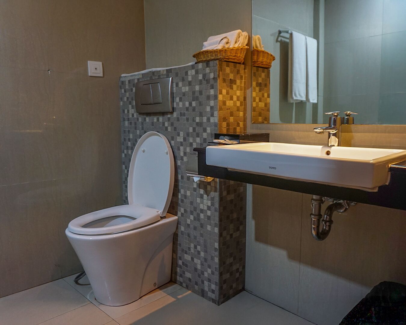 Een moderne badkamer met een wit toilet, een betegelde douchehoek, een wastafel met spiegel en een handdoekrek.