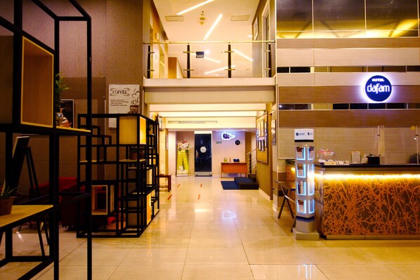 Vestíbulo de hotel con recepción, zona de estar y escalera que sube a un nivel superior.