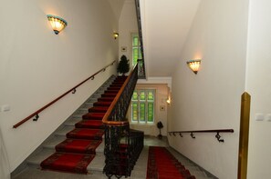 A staircase with red carpeted steps, wooden handrails, and wall-mounted light fixtures. - Hotel Sant Georg (Marianske Lazne)
