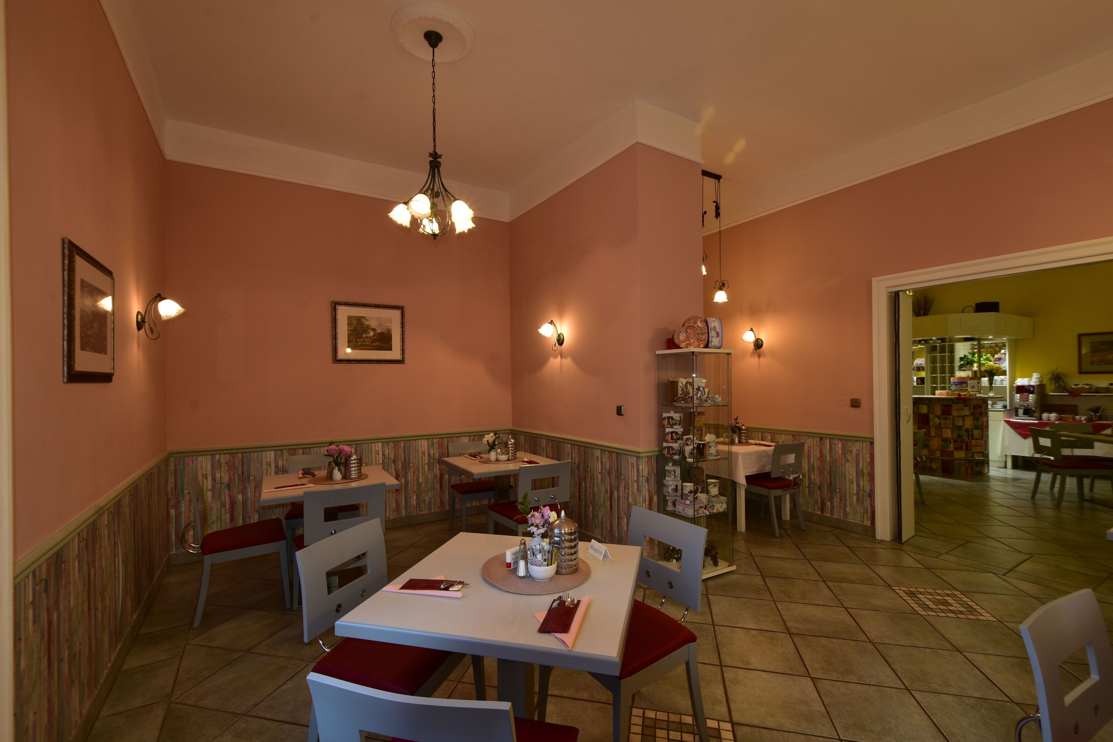 A dining area with a table set for four, chairs, a chandelier, and wall-mounted lights.