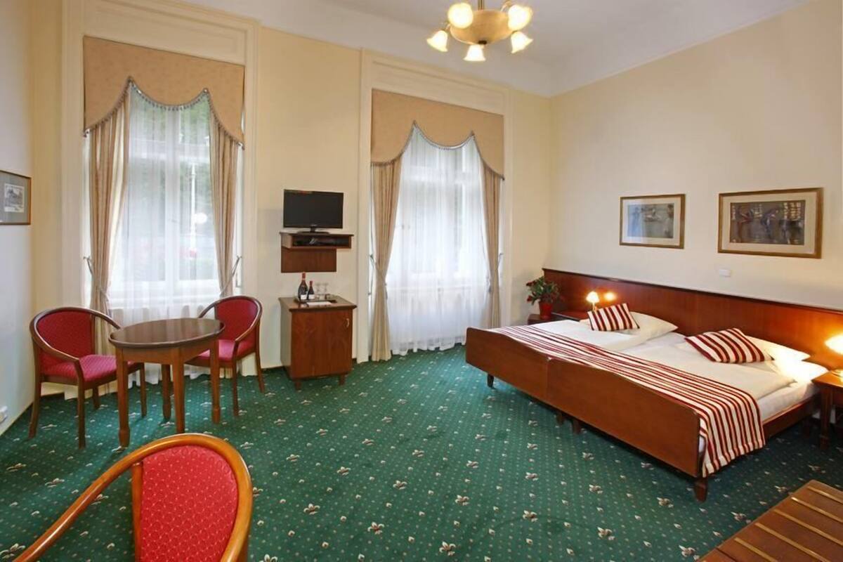 Una habitación de hotel con cama, escritorio con televisor, dos sillas y una mesita.