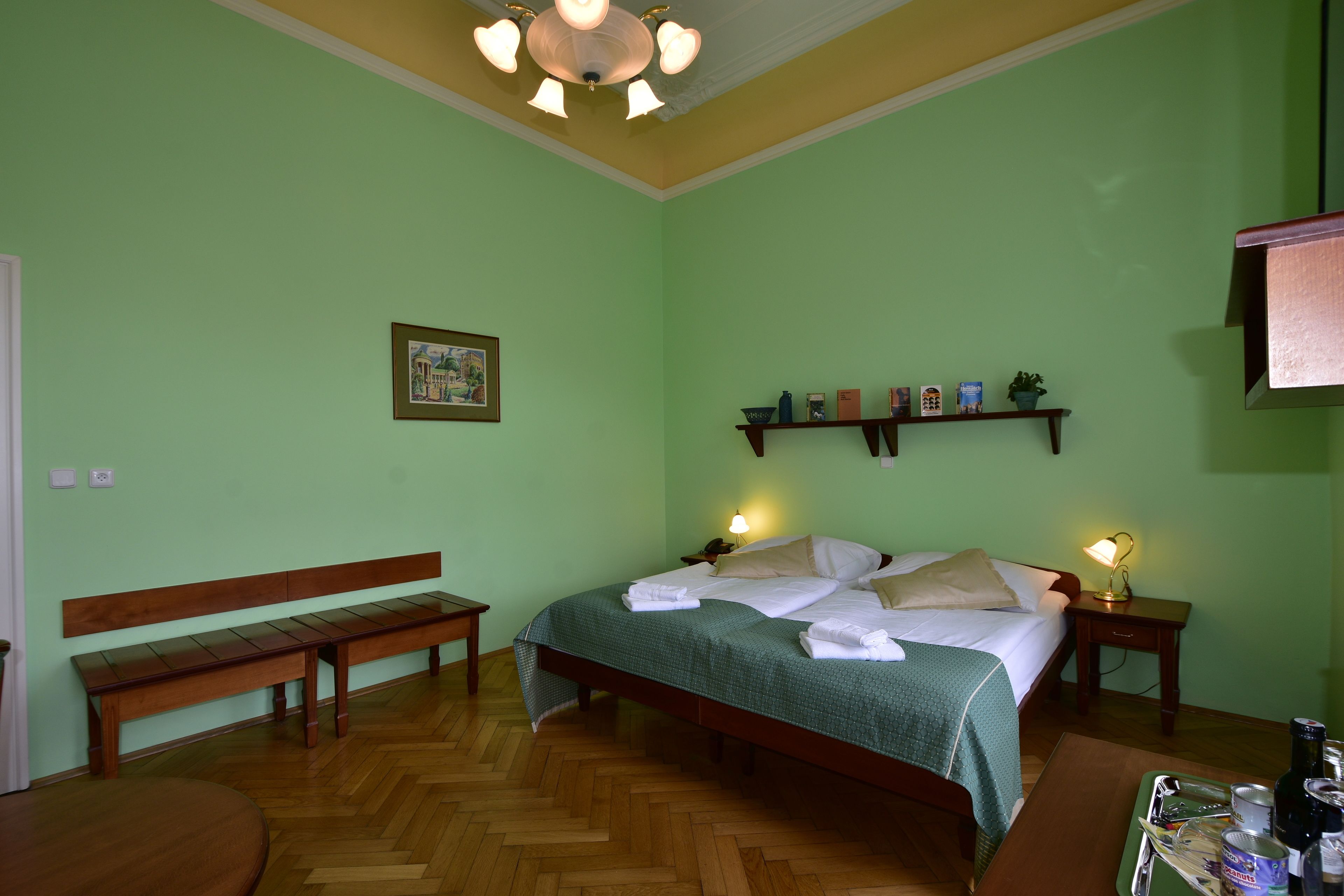 A room with a bed, a bench, a bedside table, a nightstand, and a shelf with items.