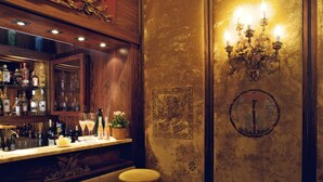 Una zona de bar con decoración de madera, una lámpara fijada a la pared y una estantería con botellas y copas.