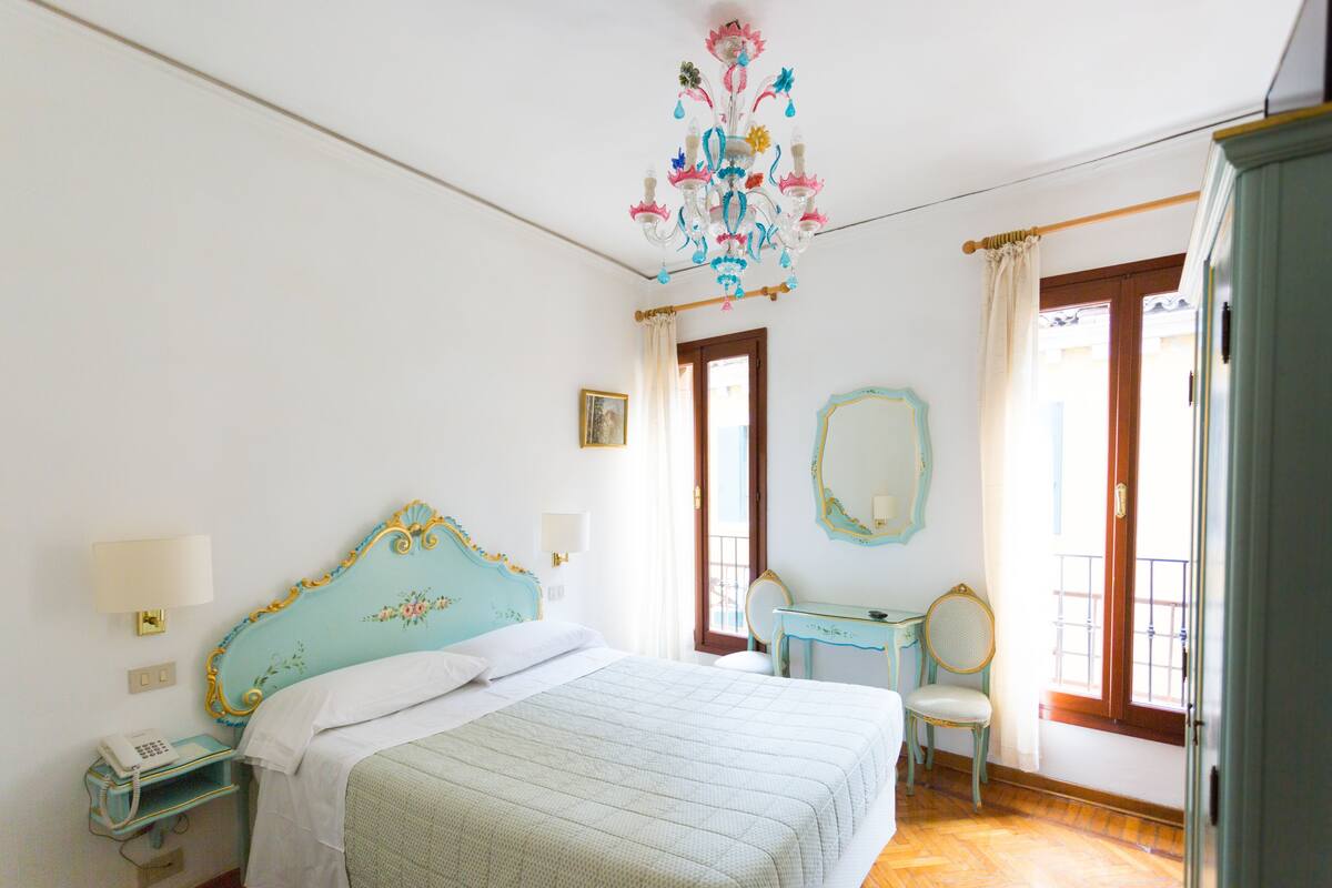 A bedroom with a bed, bedside table, chair, dresser, and a chandelier.