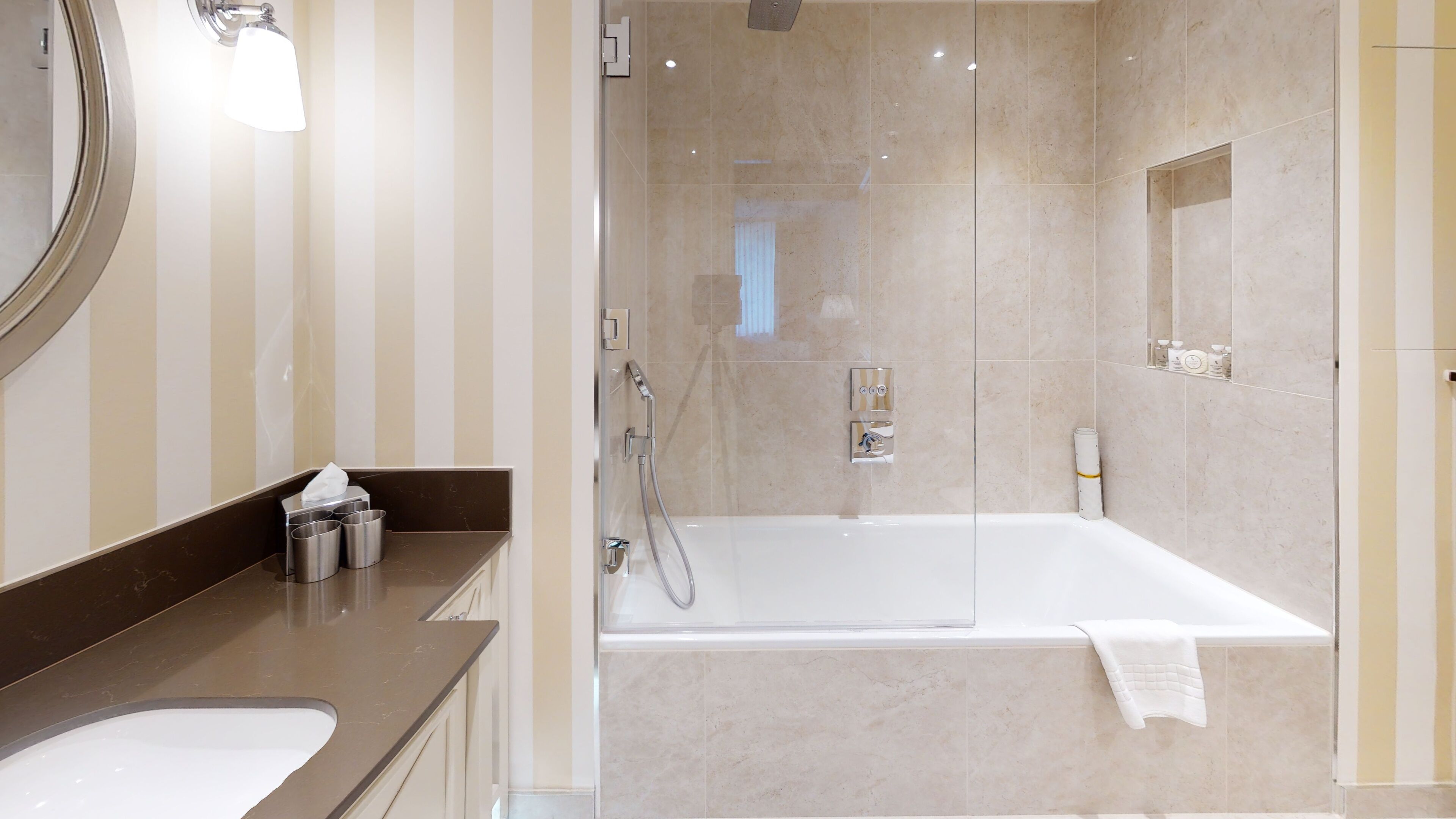 A modern bathroom with a large mirror, a bathtub, and a vanity with a sink and toiletries.