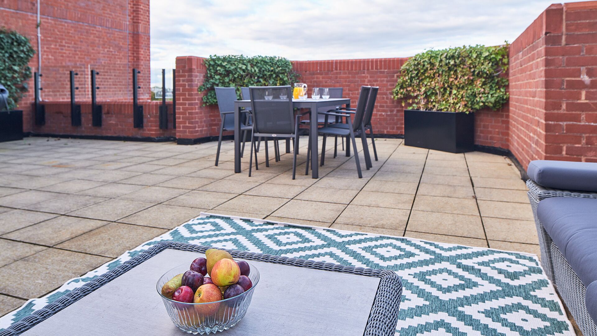 A rooftop patio with a table, chairs, and a bowl of fruit.