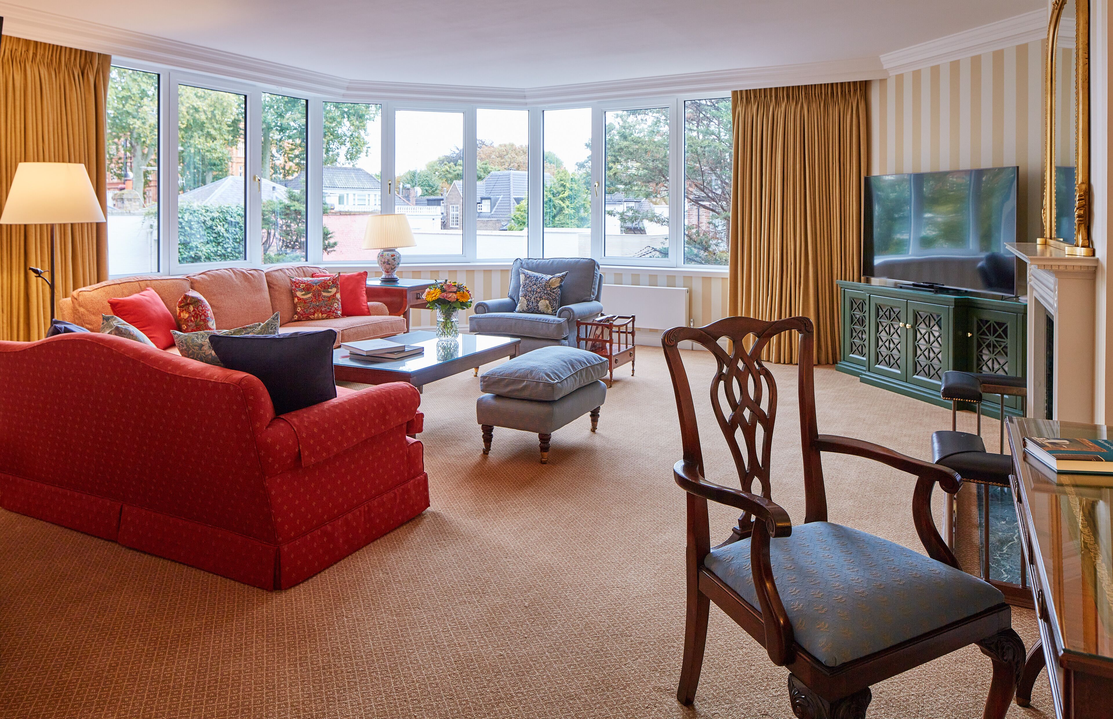 A living room with a red sofa, a blue armchair, a wooden chair, a television, and a fireplace.