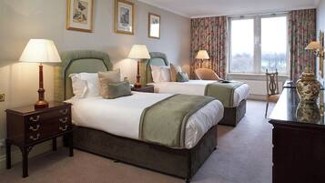 A hotel room with two beds, a dresser, lamps, and a large window with a view.