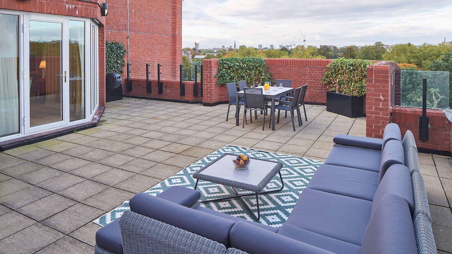 Een terras op het dak met een loungeset, een eettafel met stoelen en een bijzettafeltje met een schaal fruit.