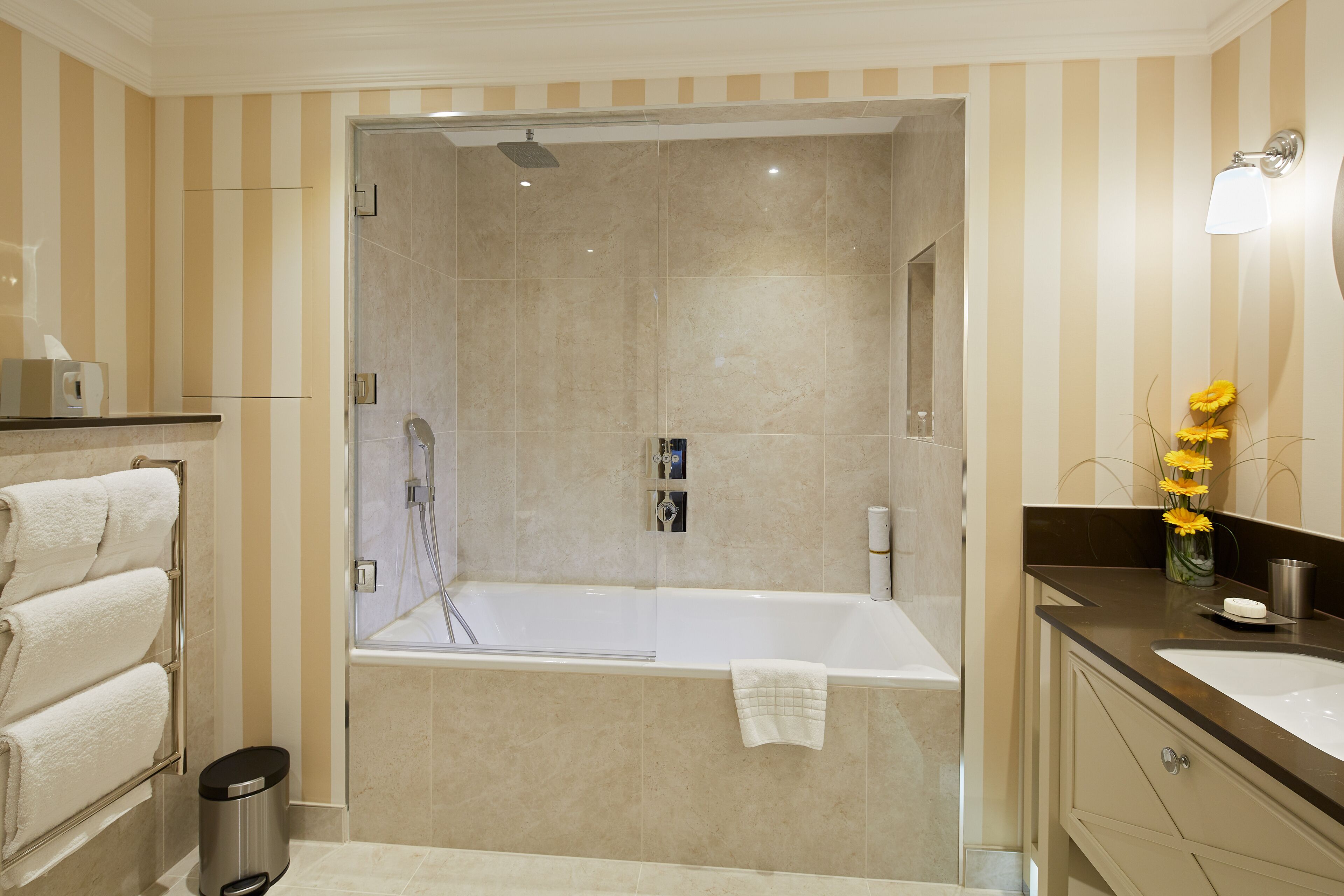 A modern bathroom with a glass-enclosed shower, a white bathtub, and a vanity with a mirror.
