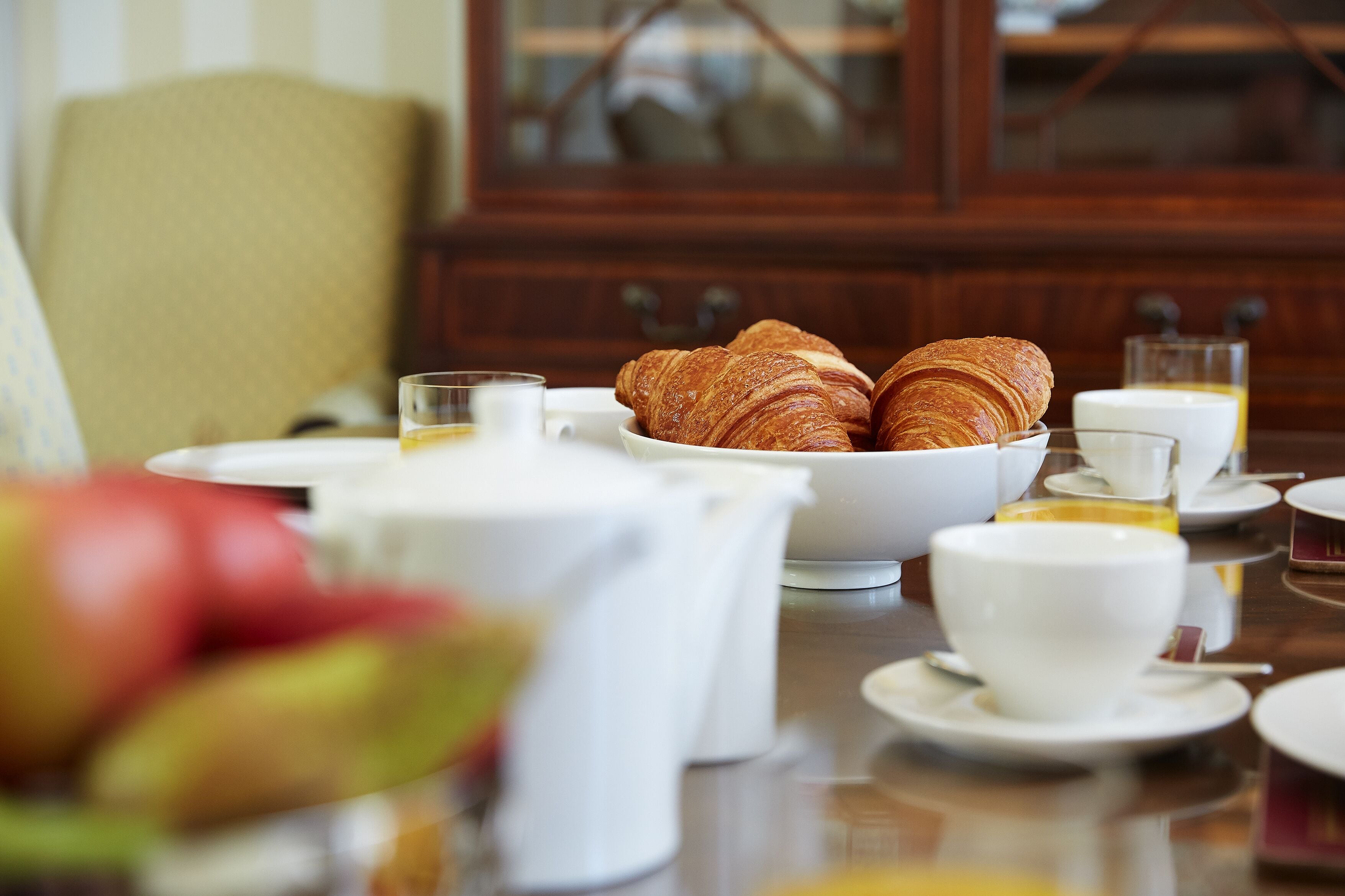 A breakfast setting with croissants, cups, and a glass of juice on a table.