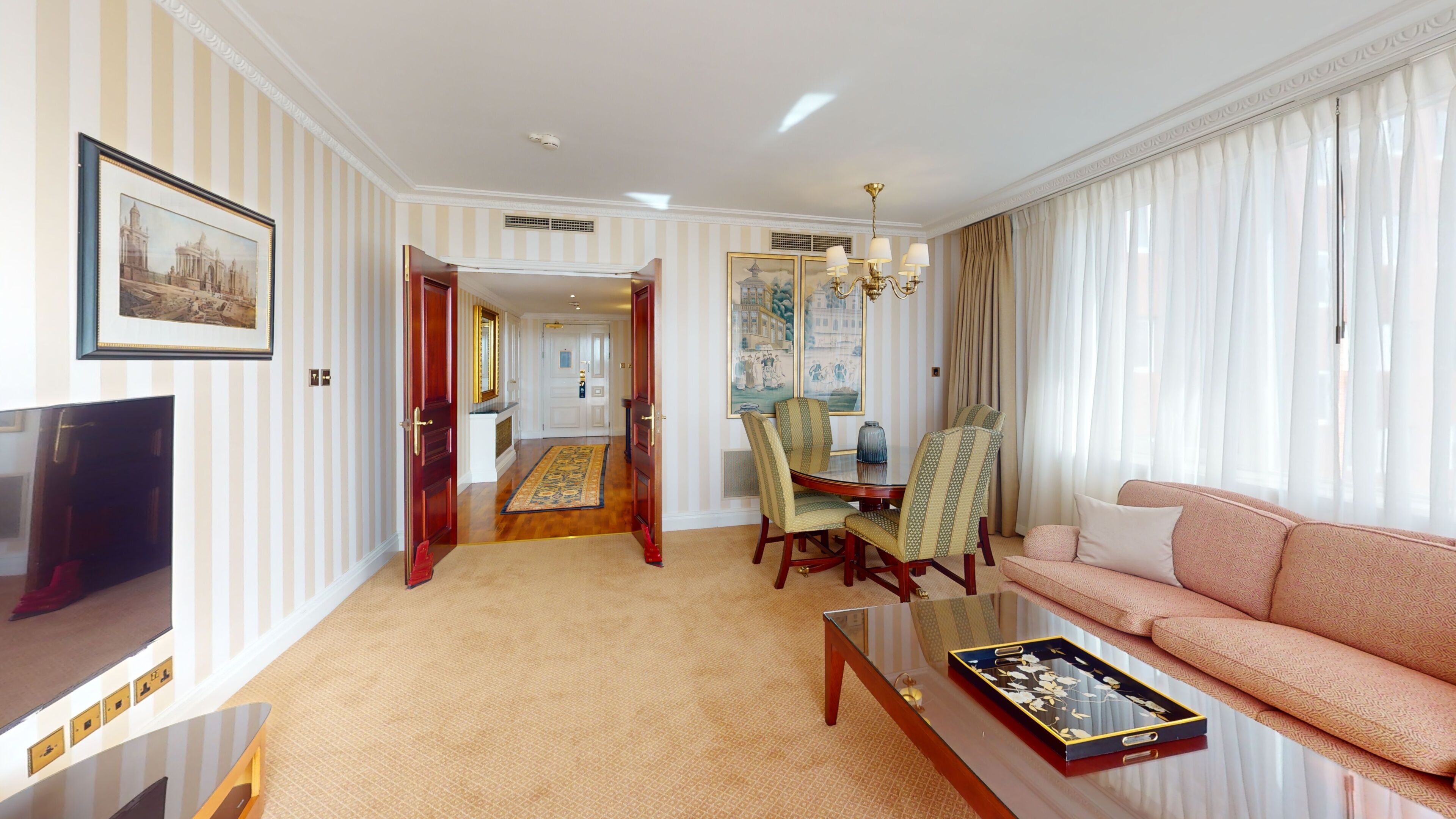 Una sala de estar con sofá, televisión, comedor con sillas y un pasillo que conduce a otra habitación.