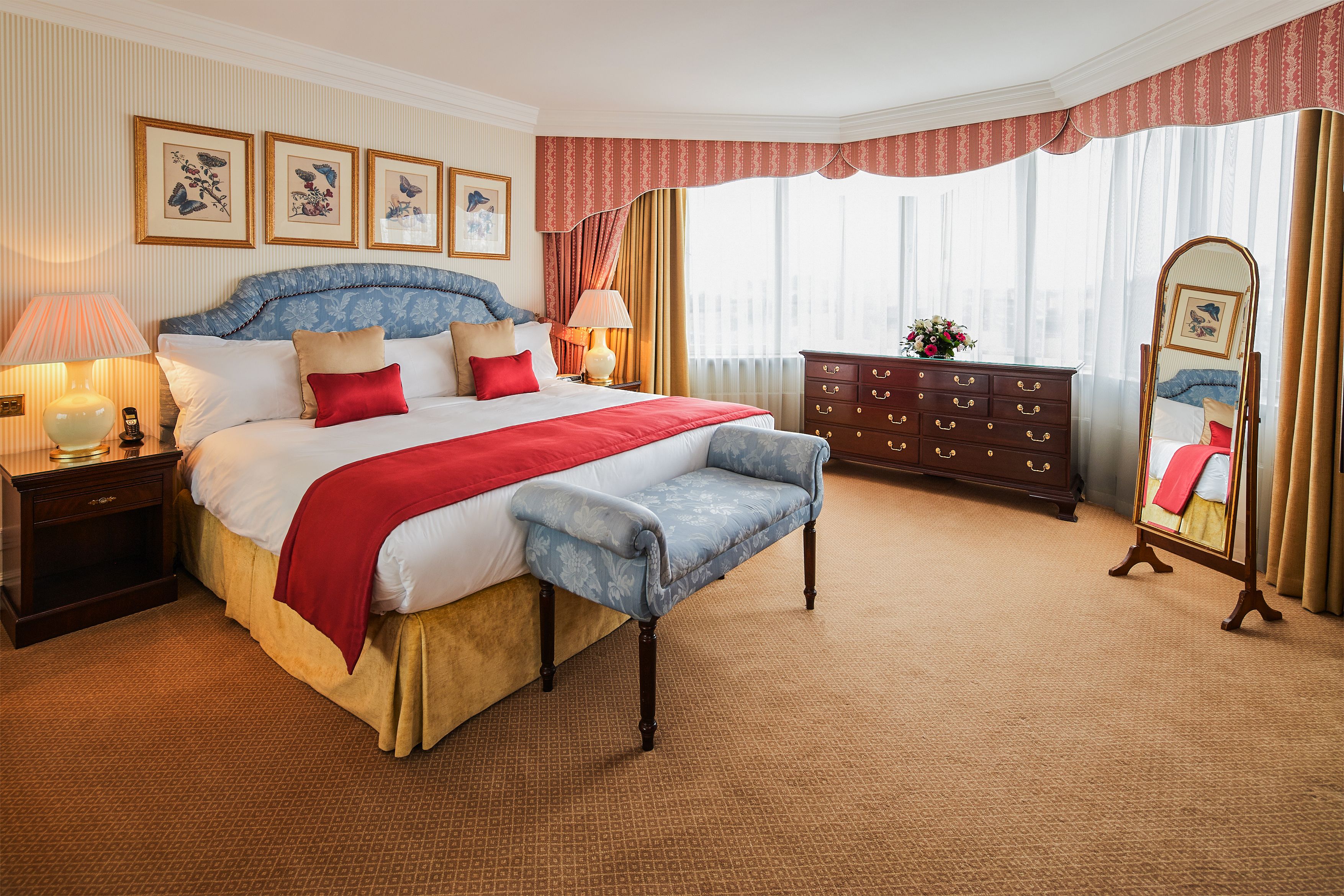 A spacious bedroom with a large bed, a nightstand, a dresser, and a full-length mirror.