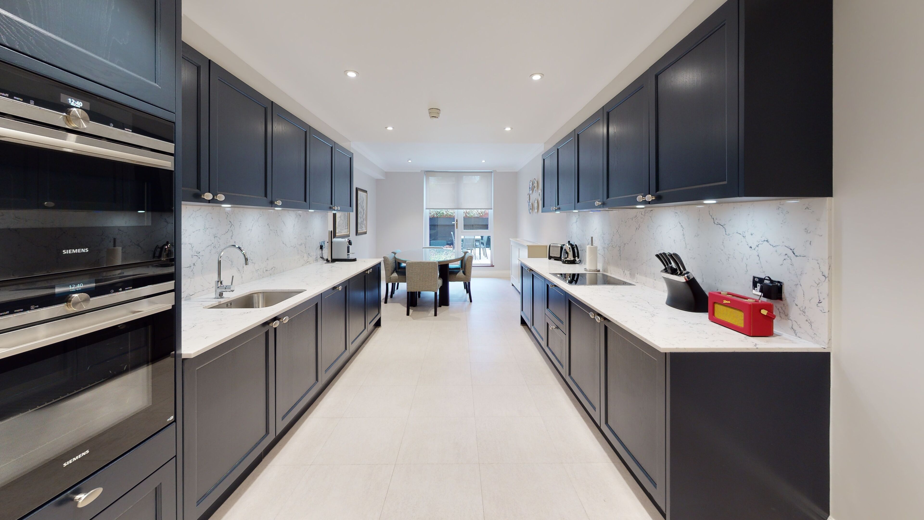 A modern kitchen with dark cabinets, a marble countertop, and a dining area with a table and chairs.