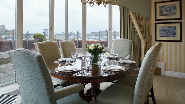 A dining room with a round table set for six, large windows, and a view of the city. - Cheval Thorney Court at Hyde Park (London)