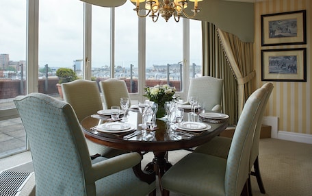 A dining room with a round table set for six, large windows, and a view of the city.