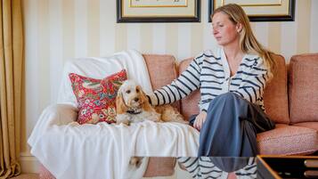 A person sitting on a patterned sofa with a dog, in a room with striped wallpaper and framed pictures on the wall.