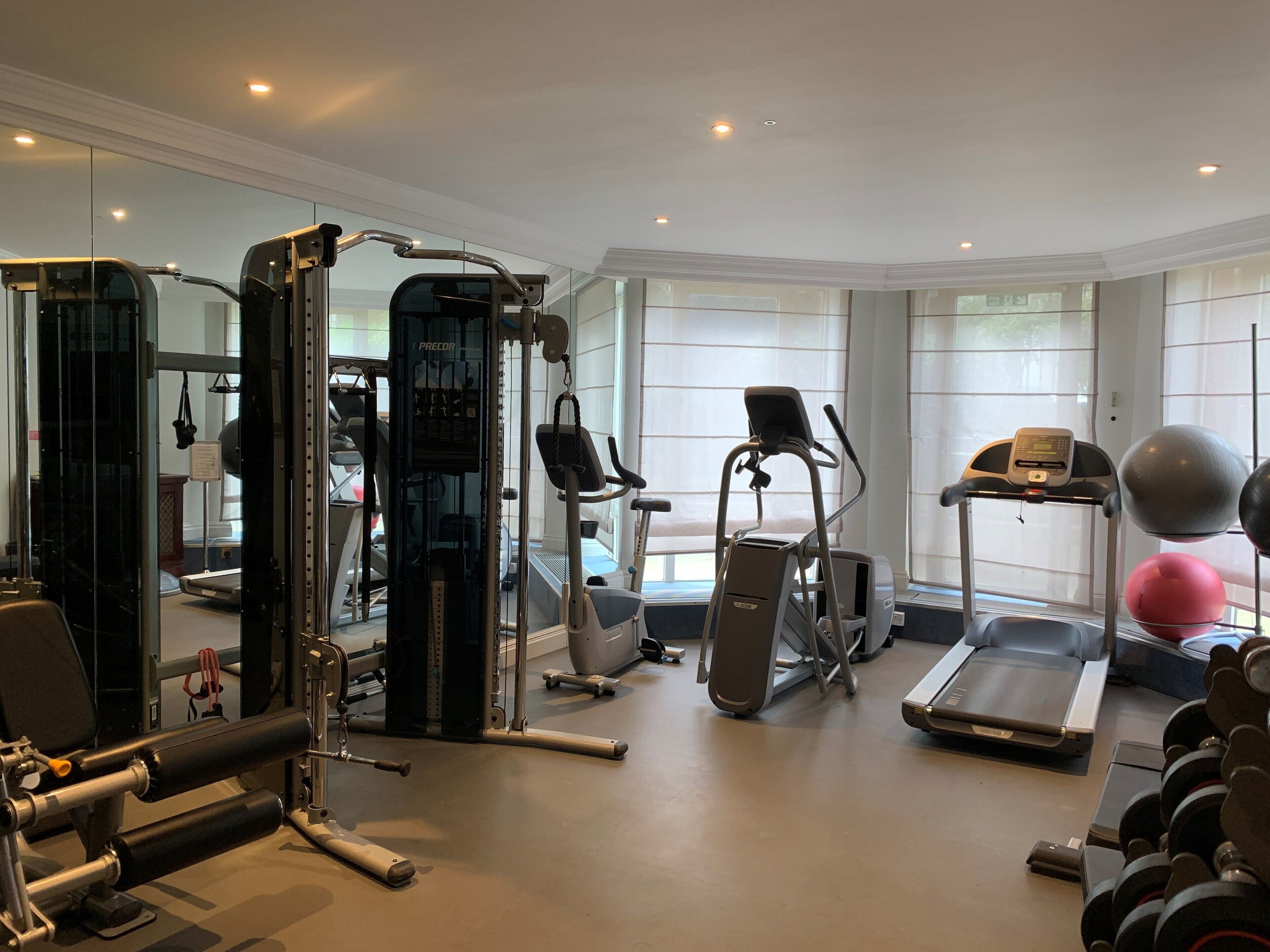 A modern gym with various exercise equipment, large windows, and a clean, spacious layout.