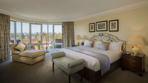 A spacious bedroom with a large bed, a sitting area, and a view of the city through large windows. - Cheval Thorney Court at Hyde Park (London)