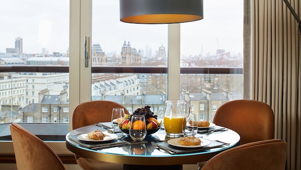 Una mesa de comedor con alimentos para el desayuno, vistas a la ciudad y una lámpara moderna.