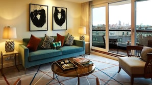 Una sala de estar moderna con un sofá azul, varios cojines, una mesa de centro y vistas a la ciudad a través de amplios ventanales.