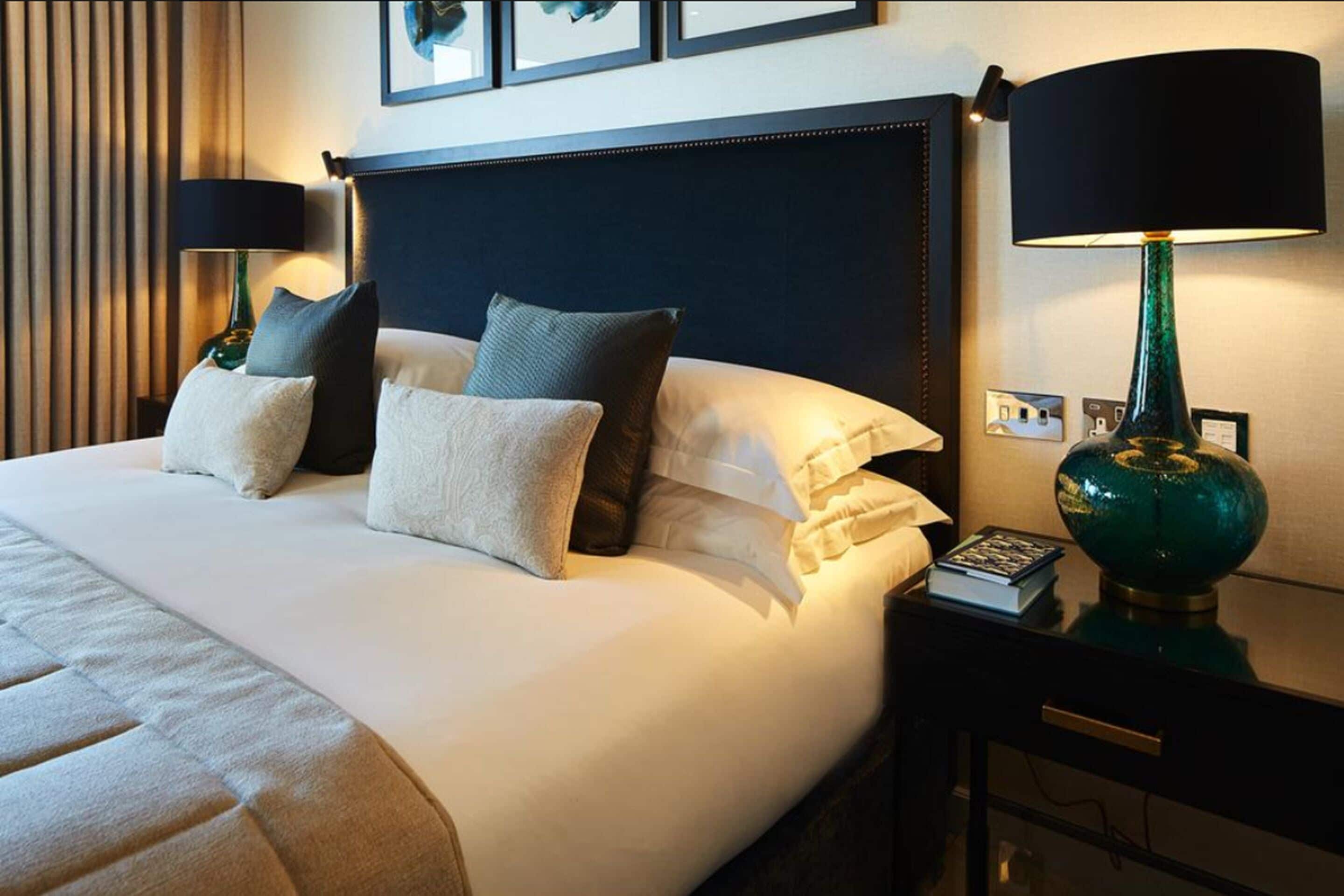 A neatly made bed with pillows, a bedside lamp, and a book on a nightstand.
