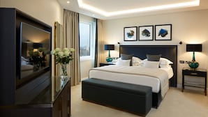 Un dormitorio de hotel moderno con una cama grande, lámparas de noche, un televisor de pantalla plana, un jarrón con flores y obras de arte en la pared.