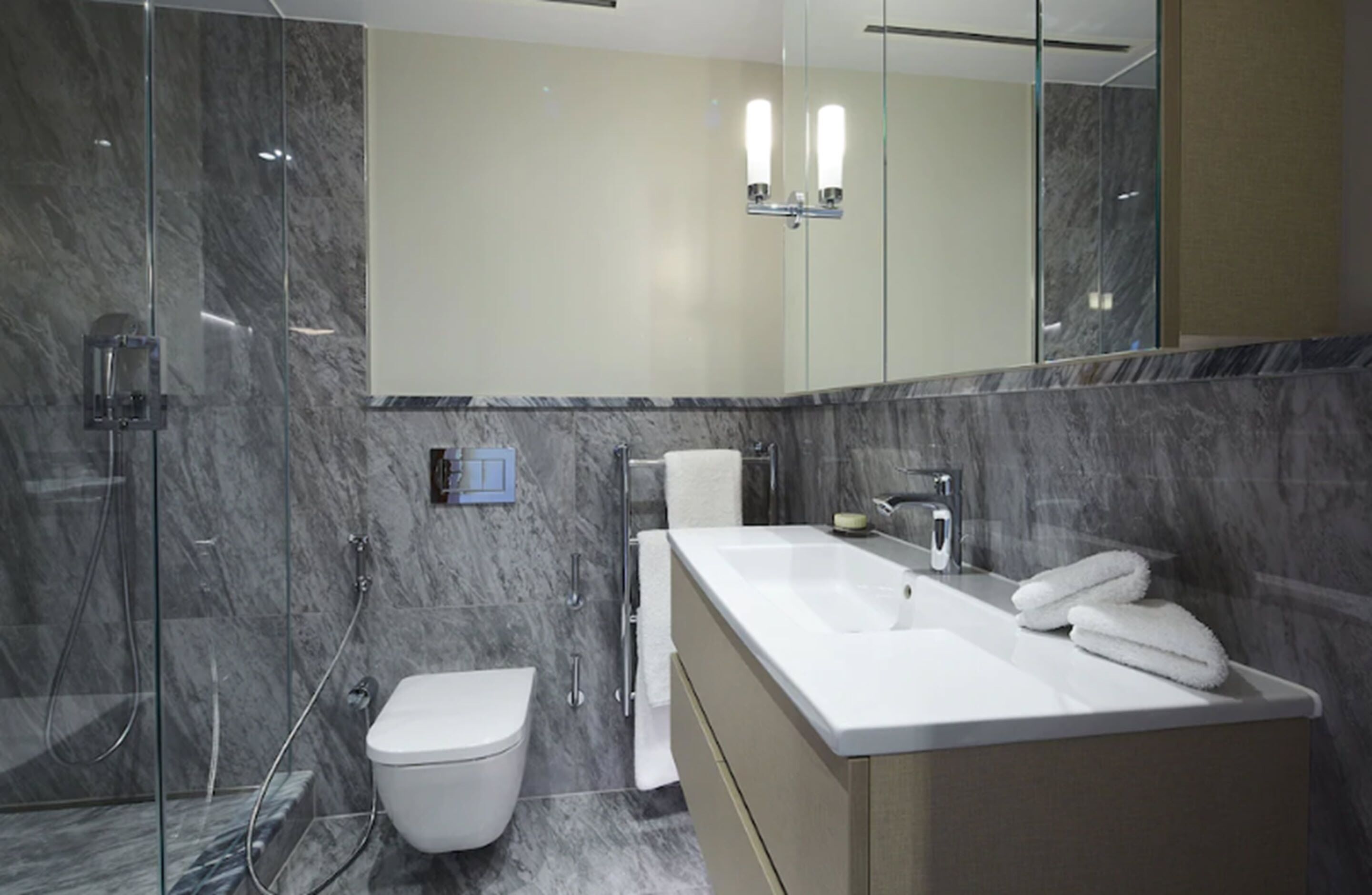 A modern bathroom with a glass shower enclosure, a white toilet, a large mirror, and a white sink with a beige cabinet.