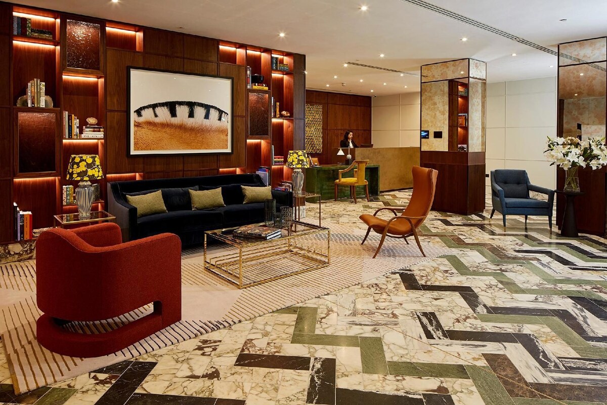 A hotel lobby with a sofa, armchairs, a reception desk, and a large painting on the wall.