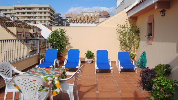 Una terrazza sul tetto con quattro poltrone blu, un tavolo con tovaglia fiorata e piante in vaso.