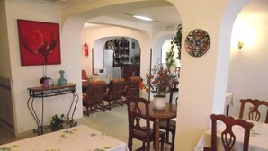 Zona pranzo con sedie e tavoli di legno, una cucina sullo sfondo e un dipinto di un fiore rosso appeso al muro.