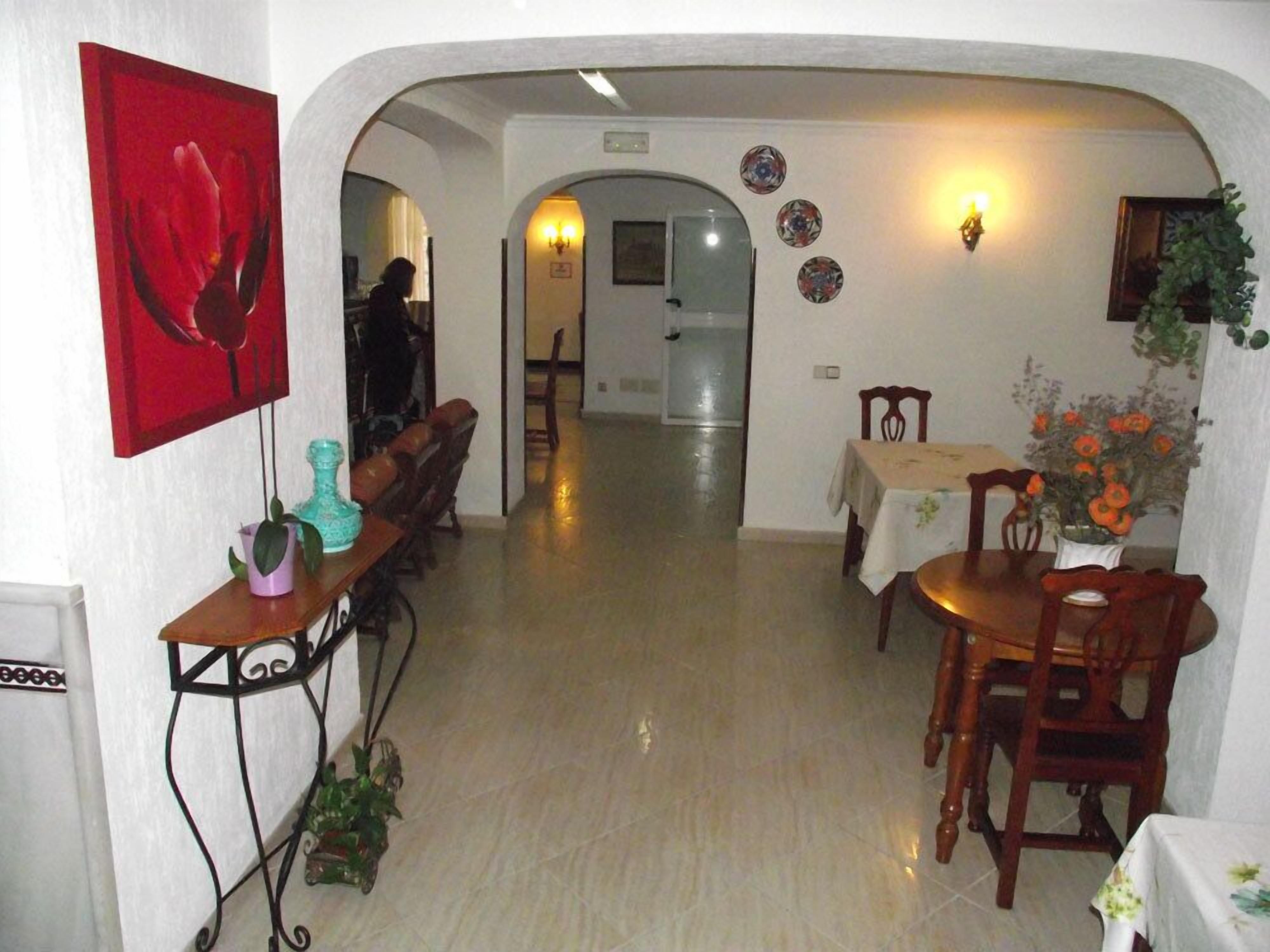 Un pasillo con una zona de comedor que incluye una mesa y sillas, una obra de arte roja en la pared y una planta en maceta.
