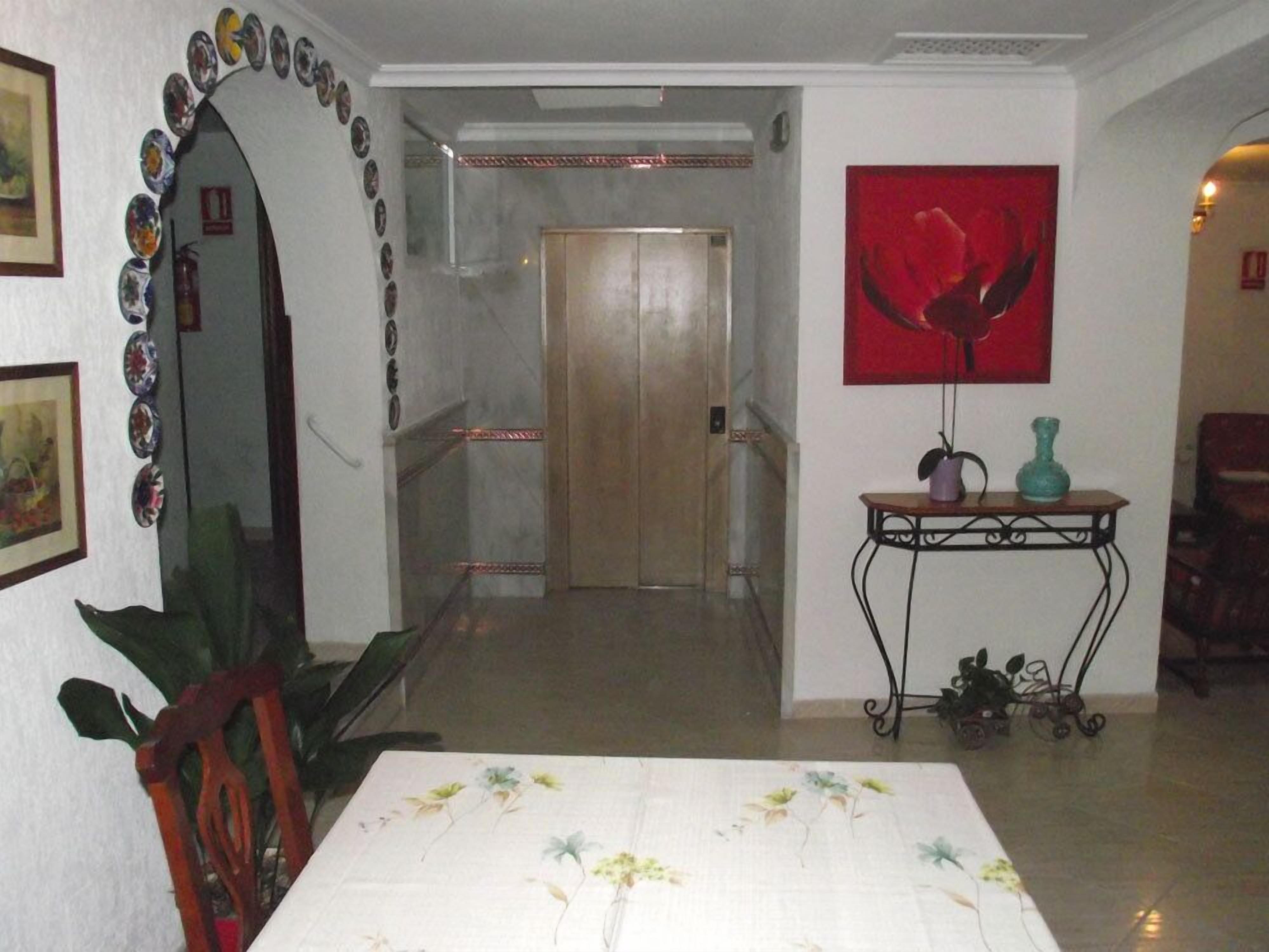 Un corridoio con una porta, un tavolo con un vaso e un quadro astratto rosso.