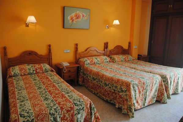 Una habitación de hotel con dos camas individuales, un cabecero de madera, una mesita de noche con un teléfono y dos lámparas fijadas a la pared.
