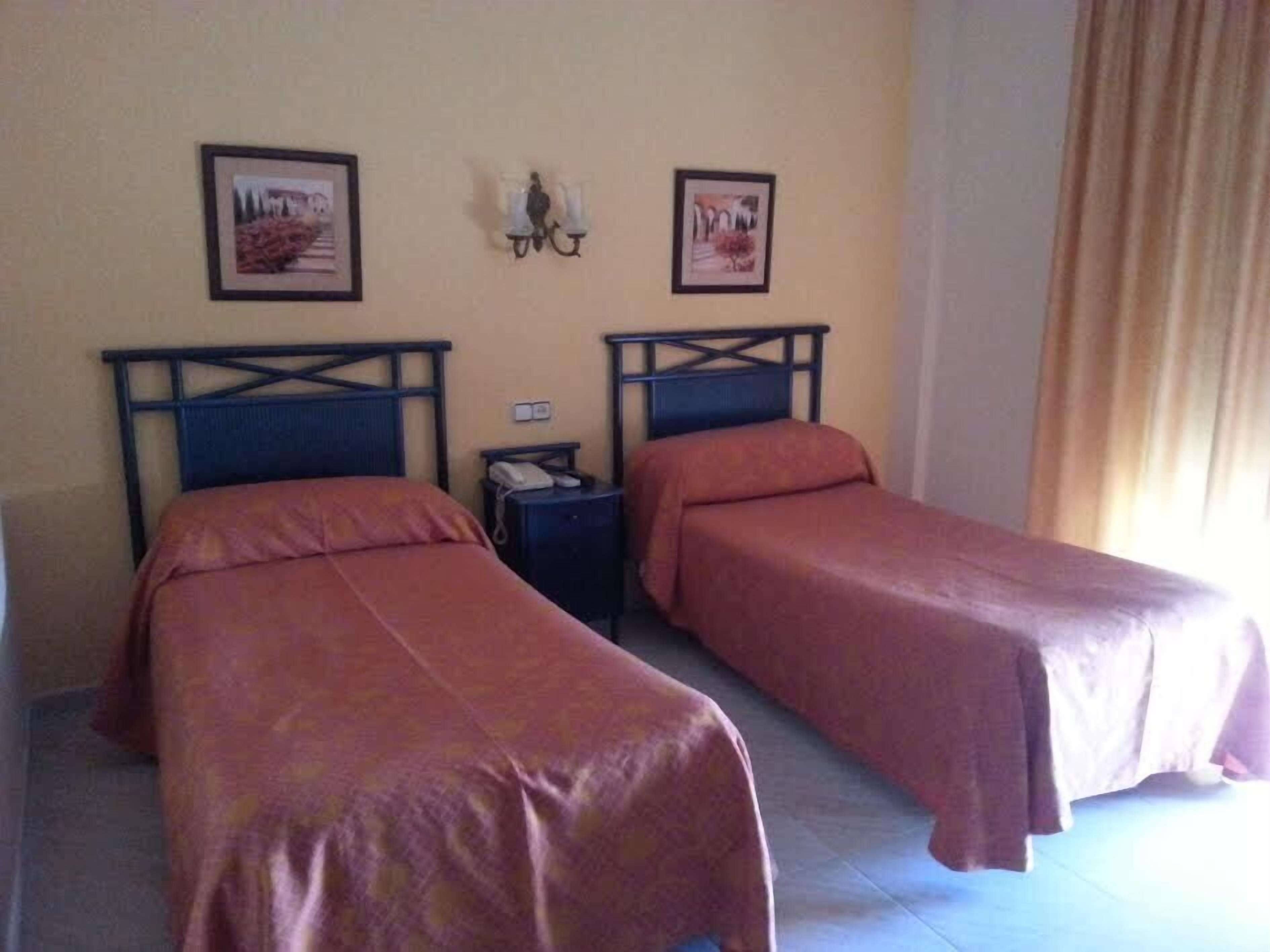 Una habitación de hotel con dos camas individuales, una mesita de noche con un teléfono y dos cuadros en la pared.