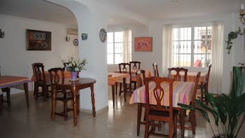 A dining area with multiple tables and chairs, a potted plant, and artwork on the walls.