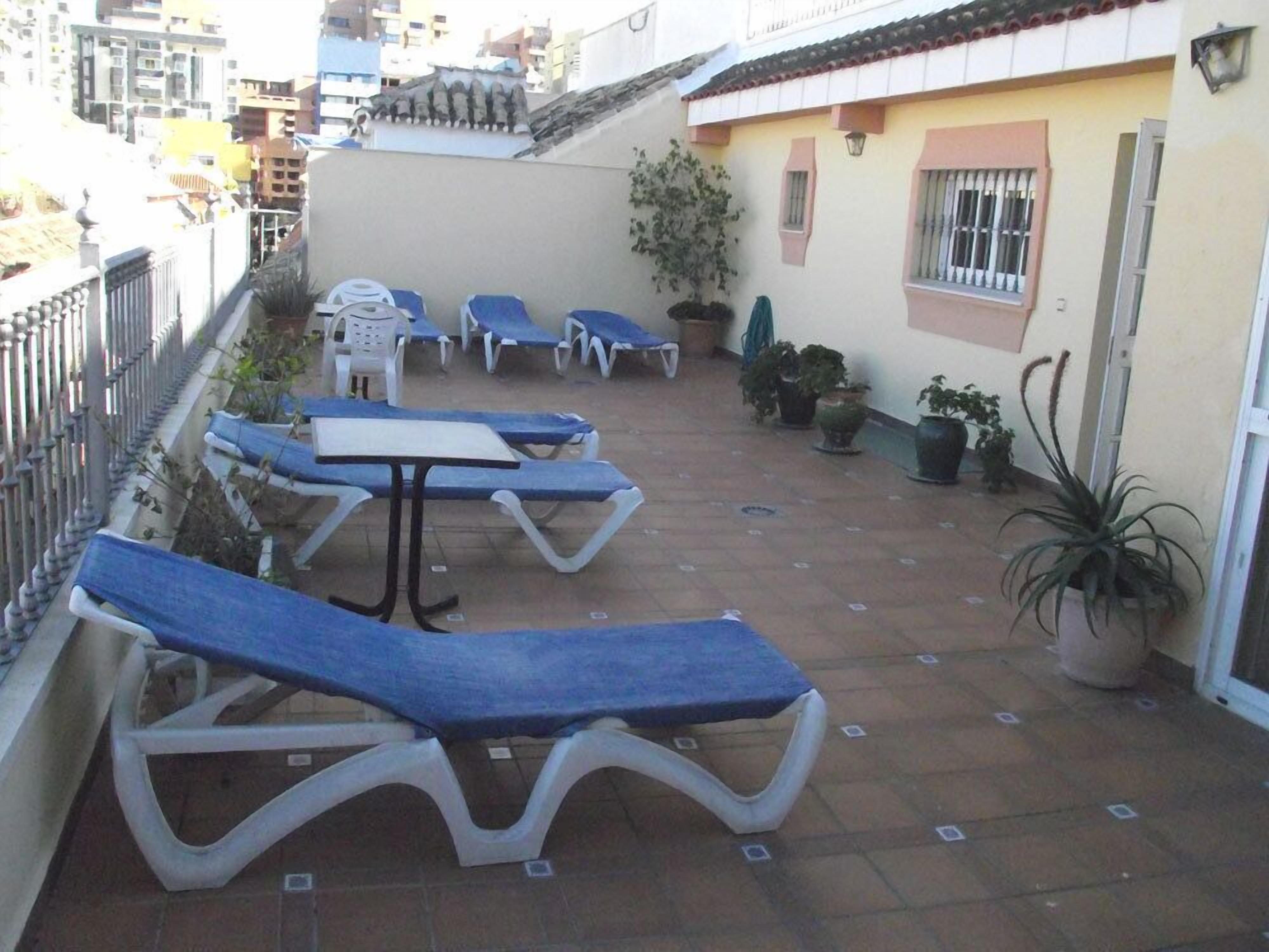 A patio with blue lounge chairs and a table, surrounded by potted plants.
