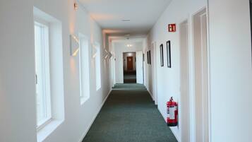 A long, narrow hallway with white walls, green carpet, and doors on both sides.
