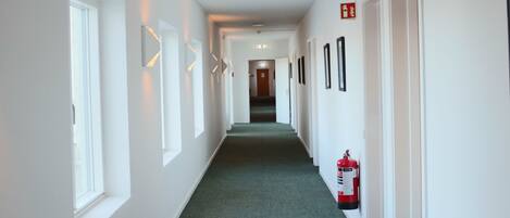 A long, narrow hallway with white walls, green carpet, and doors on both sides.