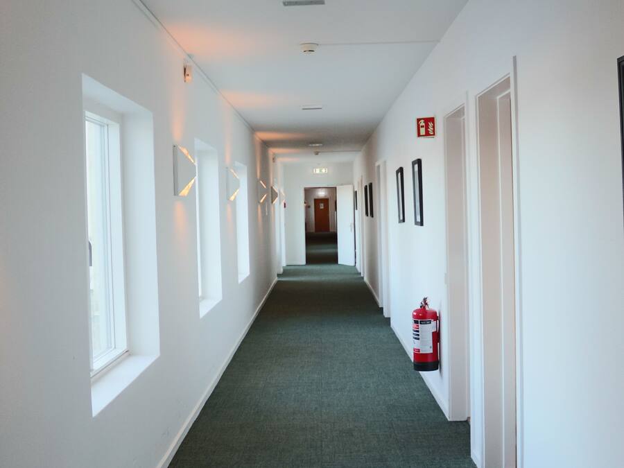 A long, narrow hallway with white walls, green carpet, and doors on both sides.