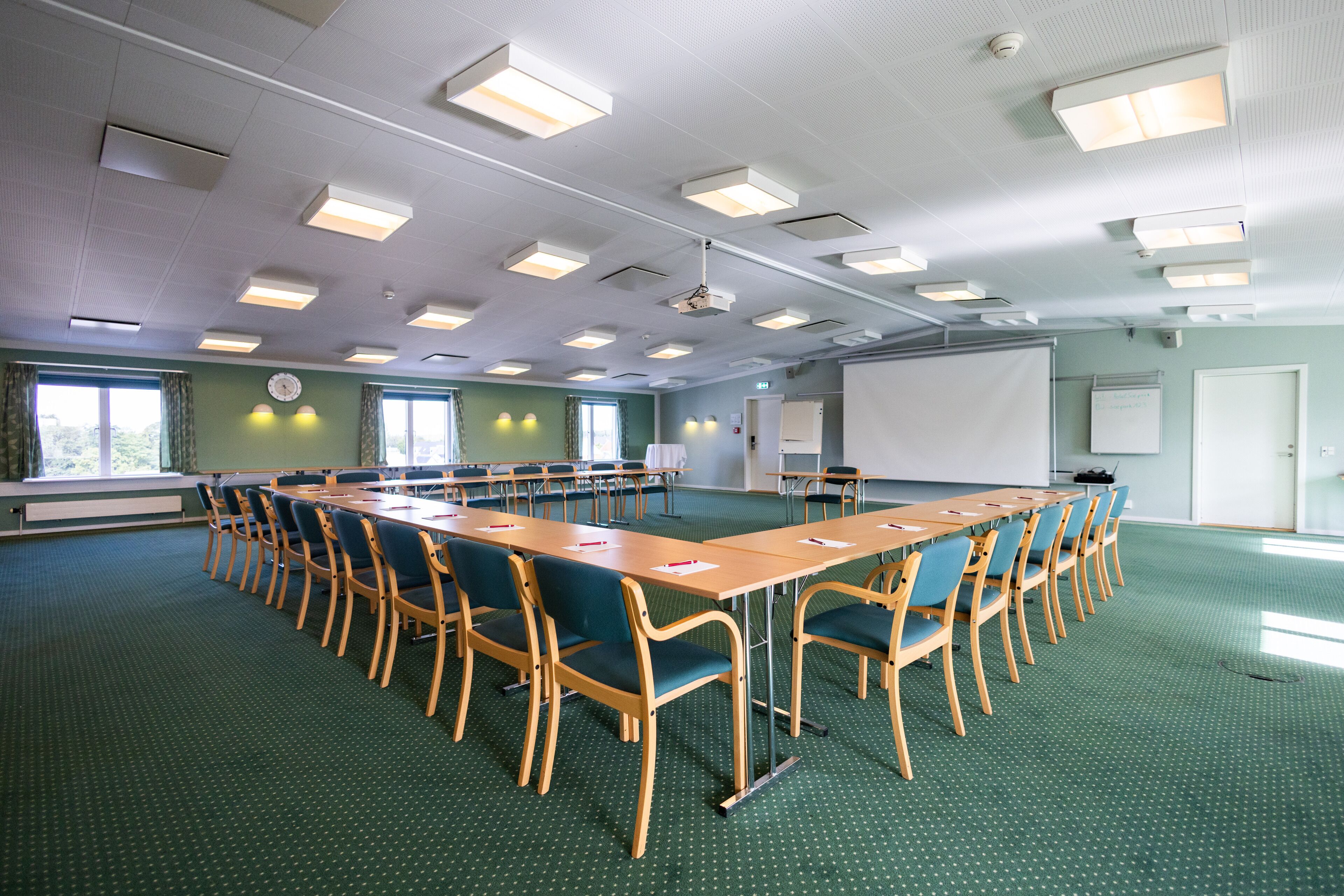 A conference room with a long table, chairs, a projector screen, and a whiteboard.
