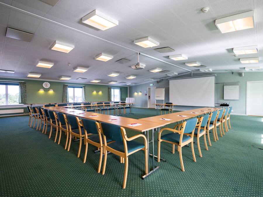 A conference room with a long table, chairs, a projector screen, and a whiteboard.