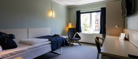 A hotel room with a bed, a desk, a chair, a lamp, and a TV.