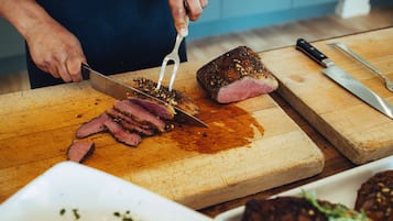 A person slicing meat on a wooden cutting board in a kitchen.