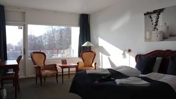 Habitación de hotel con una cama grande, dos sillones, una mesita y vistas al exterior.