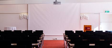Un salón de conferencias con filas de sillas, un proyector y un atril.